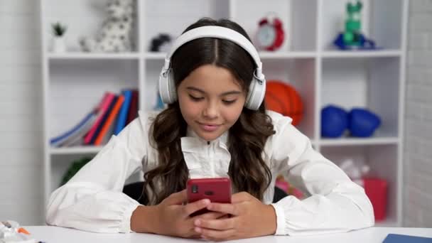 Sonriente estudiante en uniforme escolar y auriculares charlando en el teléfono móvil, navegación por Internet — Vídeos de Stock