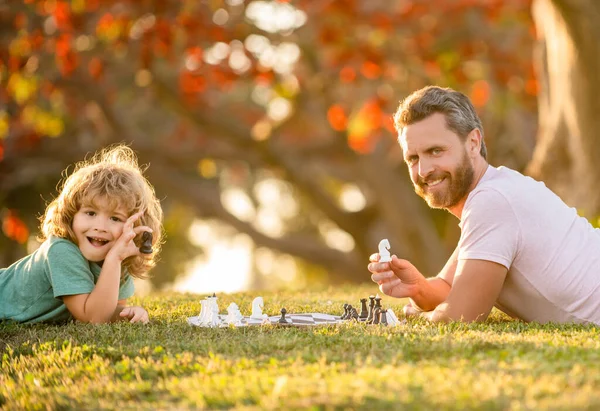 Familia feliz de padre e hijo niño jugando ajedrez sobre hierba verde en el parque al aire libre, ajedrecista — Foto de Stock