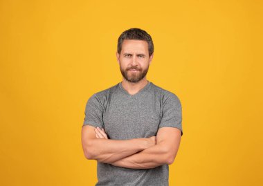Sarı arka planda gülümseyen sakallı yakışıklı, olgun kaslı adam çapraz eller, erkek güzellik