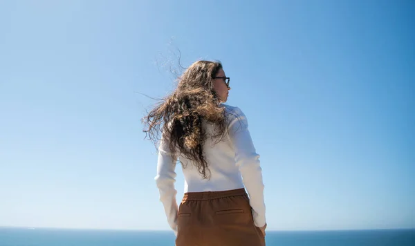 Jej włosy płyną na wietrze. Kobieta z długimi włosami stoi na morzu. Stylowa dziewczyna z falistą fryzurą — Zdjęcie stockowe