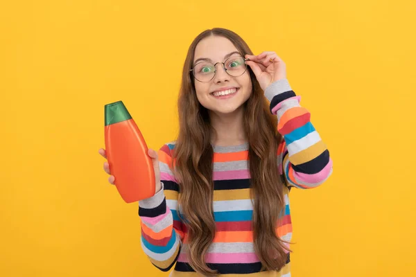 Veselé dítě dlouhé vlasy v brýlích prezentující šampón láhev, reklama — Stock fotografie