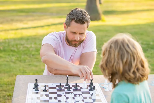 Família feliz de pai e filho criança jogando xadrez na mesa no parque ao ar livre, pensamento analítico — Fotografia de Stock