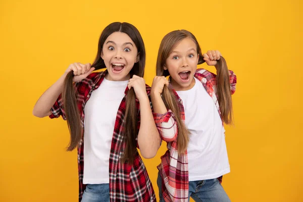 Crianças maravilhadas em camisa xadrez casual segurar cabelos longos e lisos no fundo amarelo, penteado — Fotografia de Stock