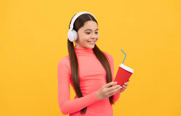 Heureux adolescent fille écouter de la musique dans les écouteurs avec tasse en papier sur fond jaune, matin — Photo