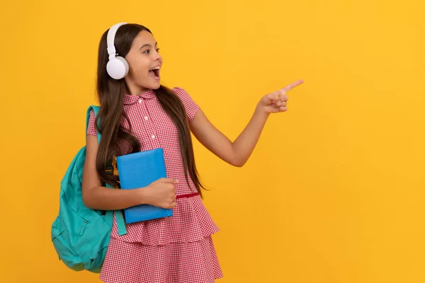Κατάπληκτος έφηβος κορίτσι σχολείο με ακουστικά δείχνουν δάχτυλο στο χώρο αντίγραφο, πίσω στο σχολείο. — Φωτογραφία Αρχείου
