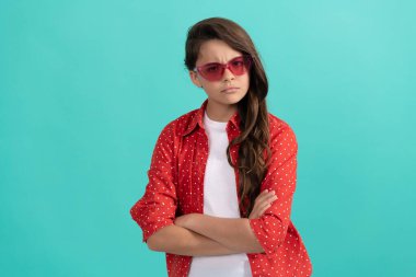 Kendine güvenen uzun kıvırcık saçlı, güneş gözlüklü, rahat gömlekli, kendine güvenen bir çocuk.