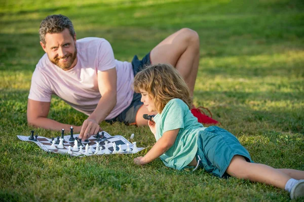 Família feliz de papai e filho criança jogando xadrez na grama verde no parque ao ar livre, xeque-mate — Fotografia de Stock