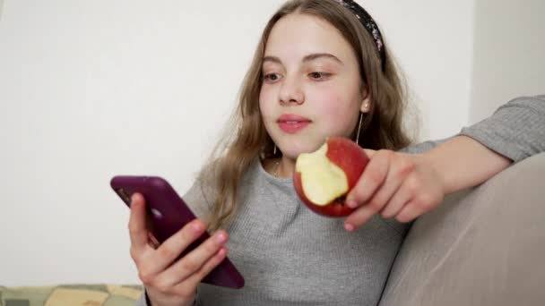 Verbaasd kind verrast met nieuws in de telefoon eet appel, emoties — Stockvideo