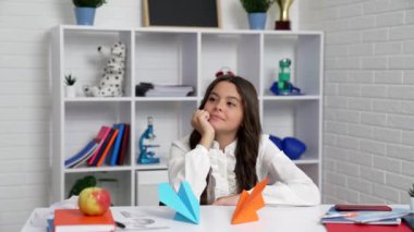 Okul üniformalı gülümseyen çocuk origami kağıt uçaklarıyla oynamaya başladı.