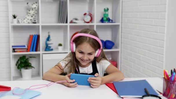 Ευτυχής κατάπληκτος έφηβος κορίτσι στα ακουστικά βλέποντας βίντεο στο smartphone στην τάξη, online εκπαίδευση — Αρχείο Βίντεο
