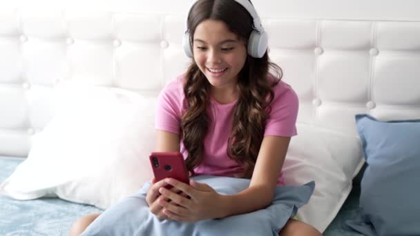Niña alegre viendo webinar en auriculares en el dormitorio, la infancia — Vídeo de stock