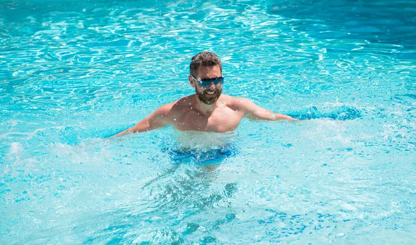 Весёлый красивый мужчина в очках, плавающий в бассейне летом, спа — стоковое фото