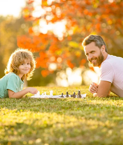 Família feliz de pai homem e filho criança jogando xadrez na grama verde no parque ao ar livre, mastermind — Fotografia de Stock
