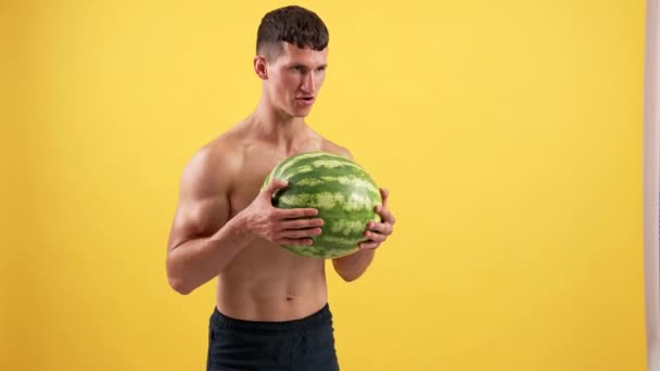 Muscular man lifting heavy water melon for biceps muscles on yellow background, sport — Stock Video