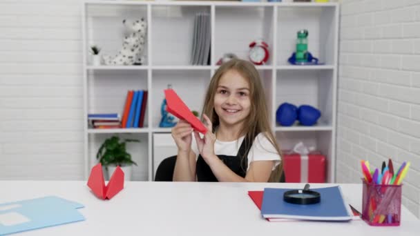 Glad skolflicka har roligt att leka med papper flygplan i skolan lektion i klassrummet, skolkamrat — Stockvideo