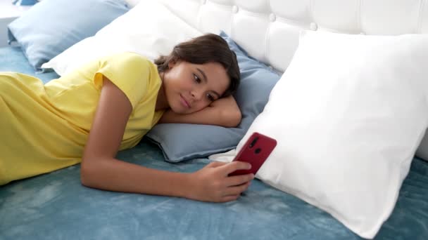 Glimlachende tiener meisje sms 'en op smartphone in bed, communicatie — Stockvideo