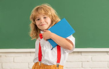 Okul sınıfında papyon takan mutlu çocuk, Eylül 'de not defteriyle ders çalışıyor.