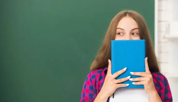 Menina adolescente no ensino médio se escondendo atrás do caderno de trabalho no quadro negro, educação — Fotografia de Stock