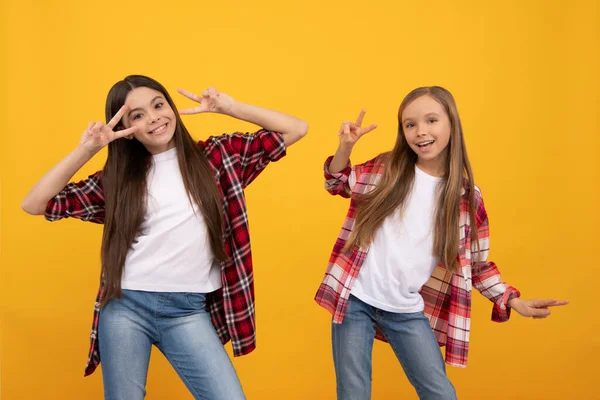 Glad tonåring flickor i ledig skjorta har kul visar fred gest på gul bakgrund, barndom. — Stockfoto