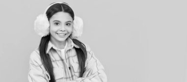 Kulaklarını sıcak tut. Paltolu mutlu kız kürk kulaklık takıyor. Kalın giysiler. Kış aksesuarları. Çocuk yüzü, yatay poster, izole edilmiş genç kız portresi, fotokopi alanı olan pankart