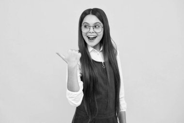 Heyecanlı bir yüz, neşeli genç bir kız. Sarı arkaplanda fotokopi alanı olan el gösteren sevimli genç kız portresi