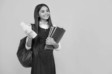 Sırt çantalı liseli kız elinde su şişesi, sarı arka planda izole halde.