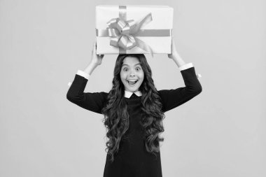 Excited face. Child with gift present box on isolated studio background. Gifting for kids birthday. Amazed expression, cheerful and glad