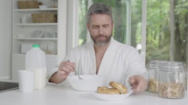 Modern mutfakta sabah kahvaltısı. Adam ev mutfağında sağlıklı kahvaltı yapıyor. Adam mutfakta kahvaltı yapıyor. Mısır gevreğini sütle yiyen adam. İspanyol adam mutfak masasında sağlıklı bir yemek yiyor..