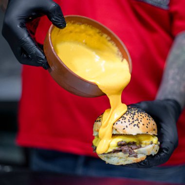 Persona con remera roja derramando queso cheddar sobre hamburguesa de carne vacuna casera
