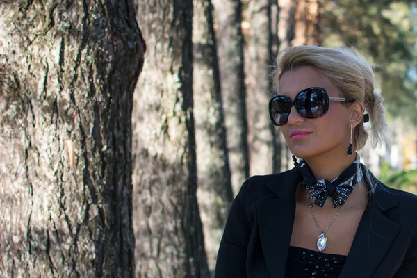 Молодая привлекательная сексуальная деловая женщина с длинными светлыми волосами, стоящая в парке. Ношение шарфа и черных очков . — стоковое фото