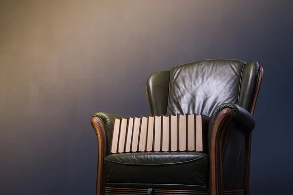 Зеленое кожаное кресло с книгами перед стеной — стоковое фото