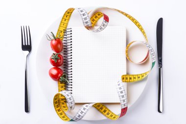 Tabak, çatal, bıçak, ölçüm bant, domates ve ahşap üzerine defter