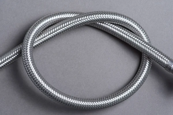 Braided stainless steel water hose over grey background — Stock Photo, Image