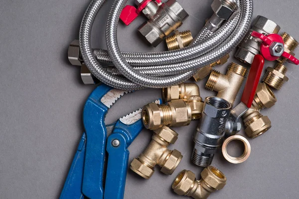 Adjustable spanner with assorted plumbing fittings and hose on grey — Stock Photo, Image