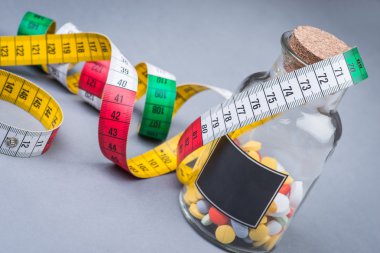 A bottle of diet pills with measuring tape clipart