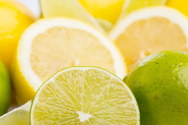 Limones y limones frescos enteros y en rodajas sobre blanco, DOF — Foto de Stock