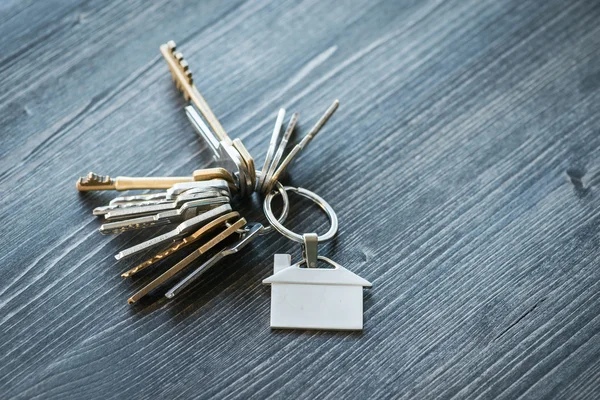 Mazzo di chiavi con portachiavi a forma di casa su un tavolo di legno — Foto Stock