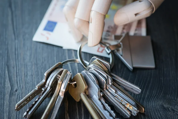 Artificial wooden hand holding the keys and money, on a wooden table — Stock Photo, Image