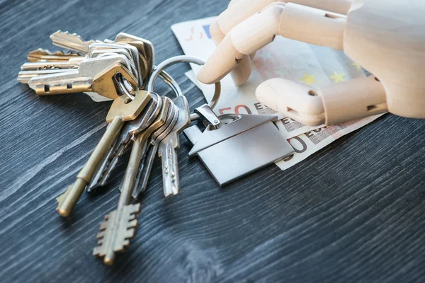 Artificial wooden hand holding the keys and money, on a wooden table — Stock Photo, Image