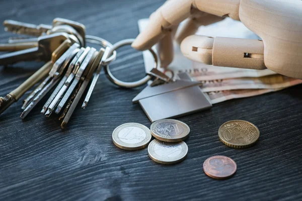 Искусственная деревянная рука, держащая ключи и деньги, на деревянном столе — стоковое фото