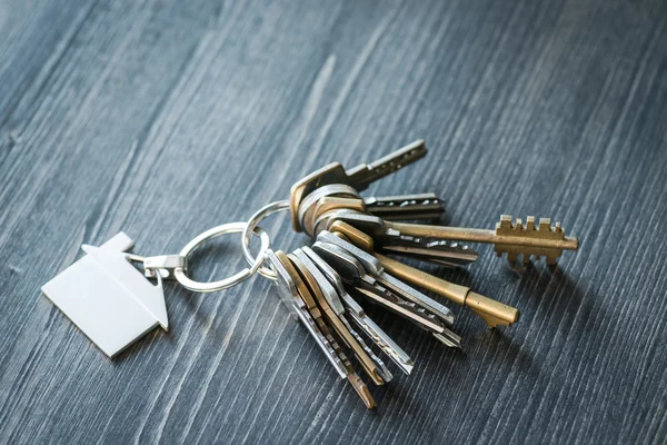 Lot de clés avec porte-clés en forme de maison sur une table en bois — Photo