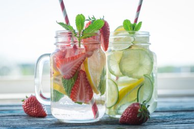Bir rustik ahşap yüzeyde su testileri limon, kireç ve çilek ile infüzyon