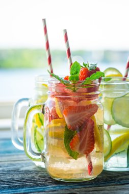 Testi ile limon, limon, çilek ve salatalık su bir rustik ahşap yüzey üzerinde infüzyon