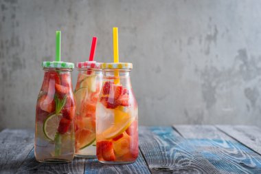 Şişe limon, limon, greyfurt ve çilek infüzyon su bir rustik ahşap yüzeye