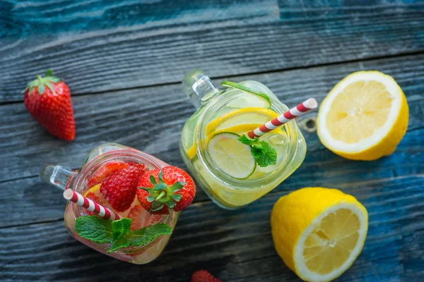 Kannen met citroen, limoen en aardbei geïnfundeerd water op een rustieke houten ondergrond — Stockfoto