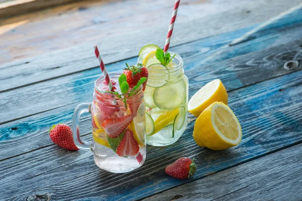 Bir rustik ahşap yüzeyde su testileri limon, kireç ve çilek ile infüzyon