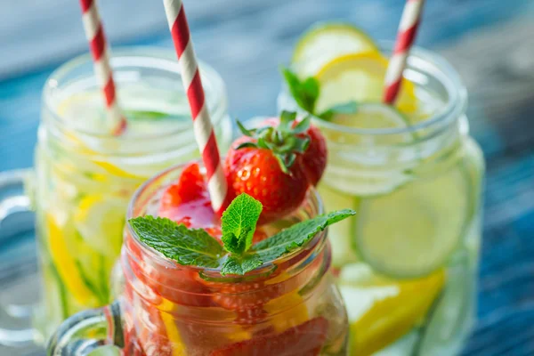 Jugs with lemon, lime, strawberry and cucumber infused water on a rustic wooden surface — Stock Photo, Image