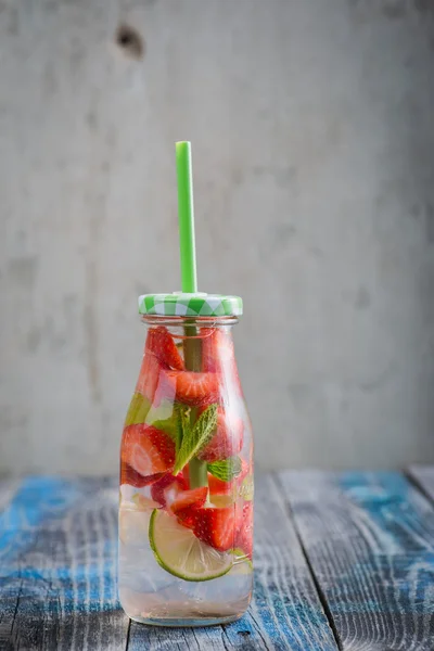 Flaska med lime och jordgubbar infunderas vatten på en rustik trä yta — Stockfoto