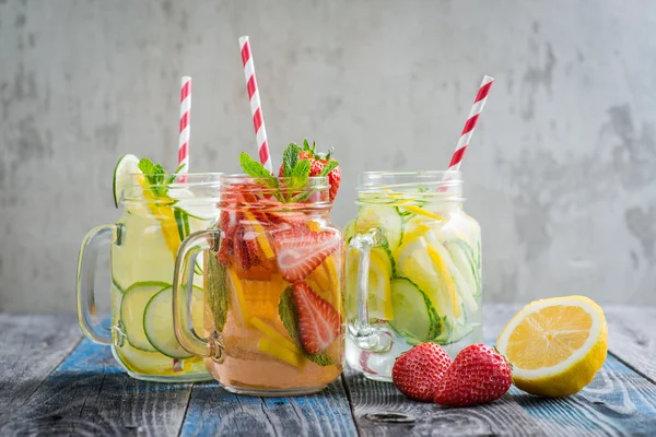 Krüge mit Zitronen-, Limetten-, Erdbeer- und Gurkenwasser auf rustikaler Holzoberfläche — Stockfoto