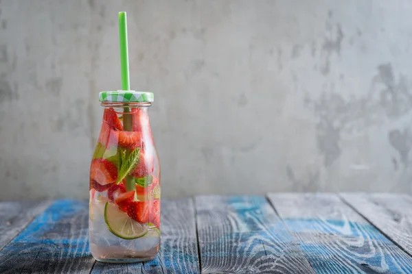 Flaske med kalk og jordbær infunderet vand på en rustik træoverflade - Stock-foto